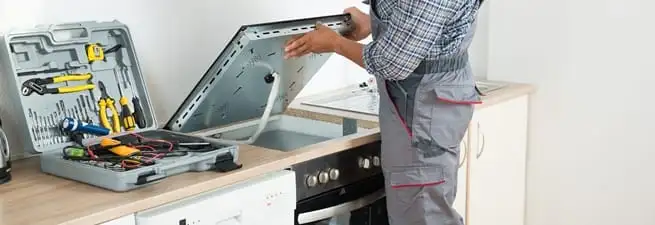 Cooktop repair technician lifting a built-in stovetop for service in Boulder, CO