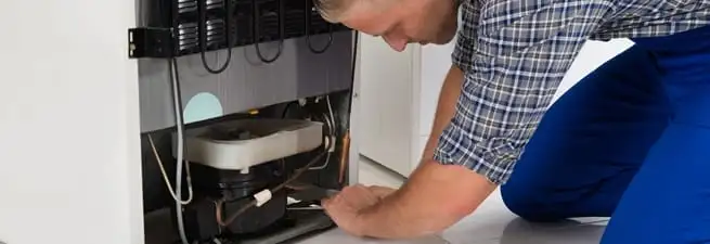 Refrigerator repair technician servicing the compressor and condenser area in Boulder, CO