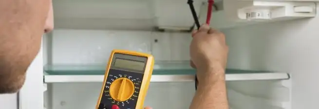 Refrigerator repair technician testing electrical components with a multimeter in Boulder, CO