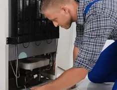 Refrigerator repair technician servicing the compressor and condenser area in Boulder, CO